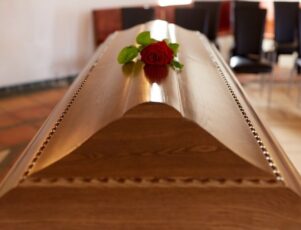 Em dúvida sobre entre caixão fechado ou aberto? Saiba mais! Uma rosa vermelha solitária sobre um caixão de madeira escuro, ilustrando um caixão fechado.