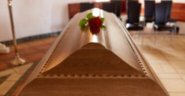 Uma rosa vermelha solitária sobre um caixão de madeira escuro, ilustrando um caixão fechado.