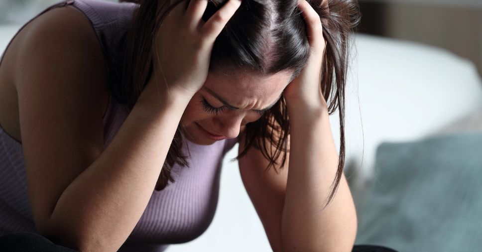 Mulher chora com as mãos na cabeça, representando a dor do luto antecipatório.