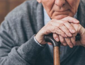 Saiba como lidar com o luto na terceira idade! Close em mãos de idoso apoiadas sobre bengala ilustra o luto na terceira idade.