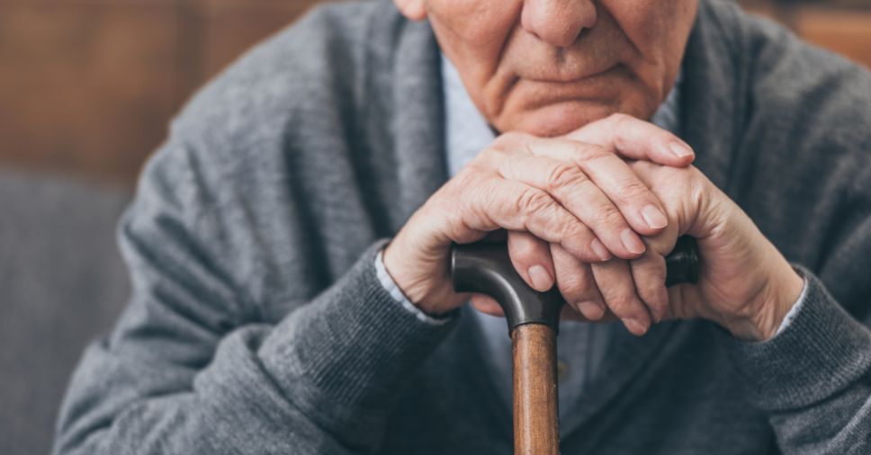Close em mãos de idoso apoiadas sobre bengala ilustra o luto na terceira idade.
