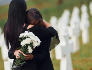 Conforto e acolhimento no luto familiar é na Funerária Pax Rio 24H Duas mulheres abraçam-se num cemitério enquanto seguram flores, em meio ao suporte no luto familiar.